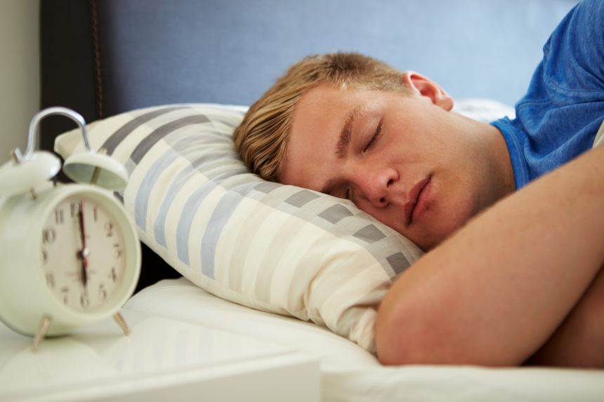 A teenage boy having an early night the night before an exam with an alarm clock set on the bedside table.