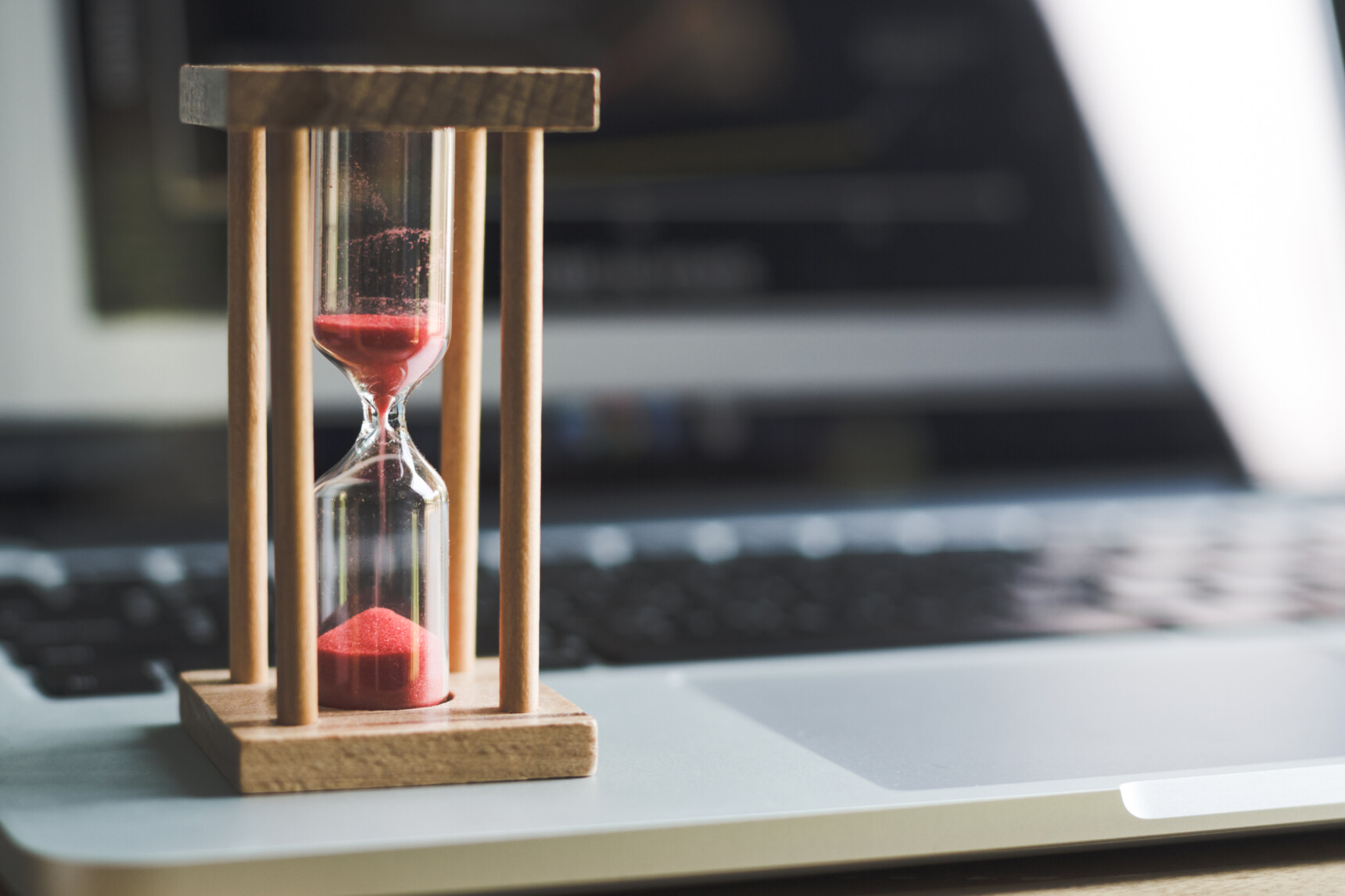 An hourglass placed on top of a laptop.