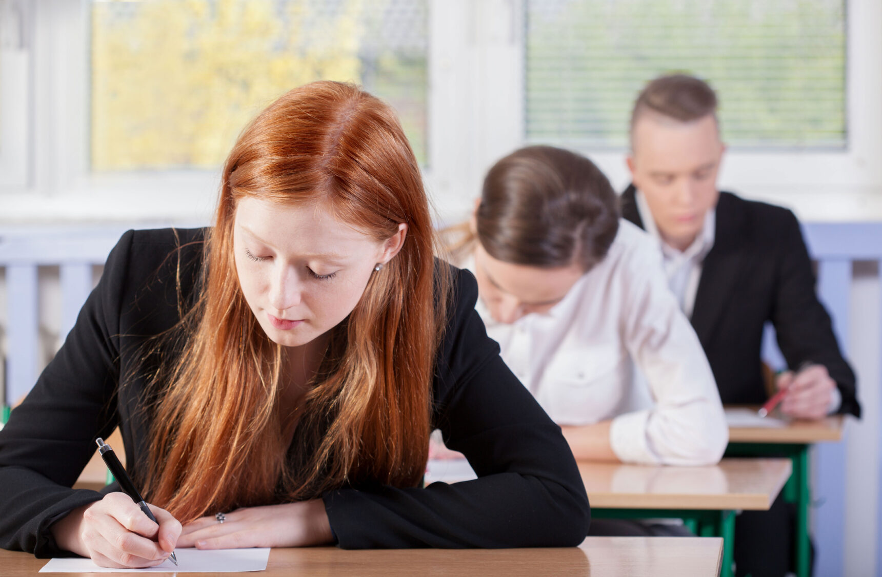 A group of A Level students are sitting at desks writing as they take an A Level exam.