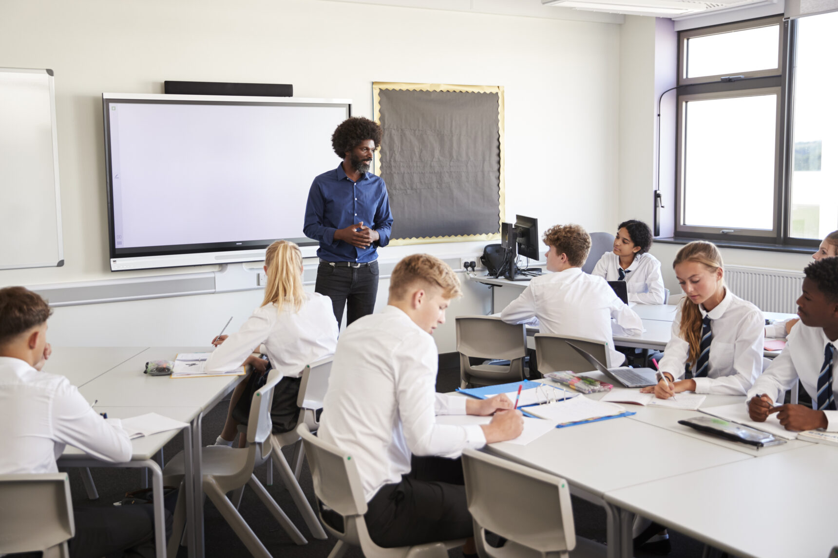 A male teacher putting pedagogy into practice as he teaches a group of students in a classroom.
