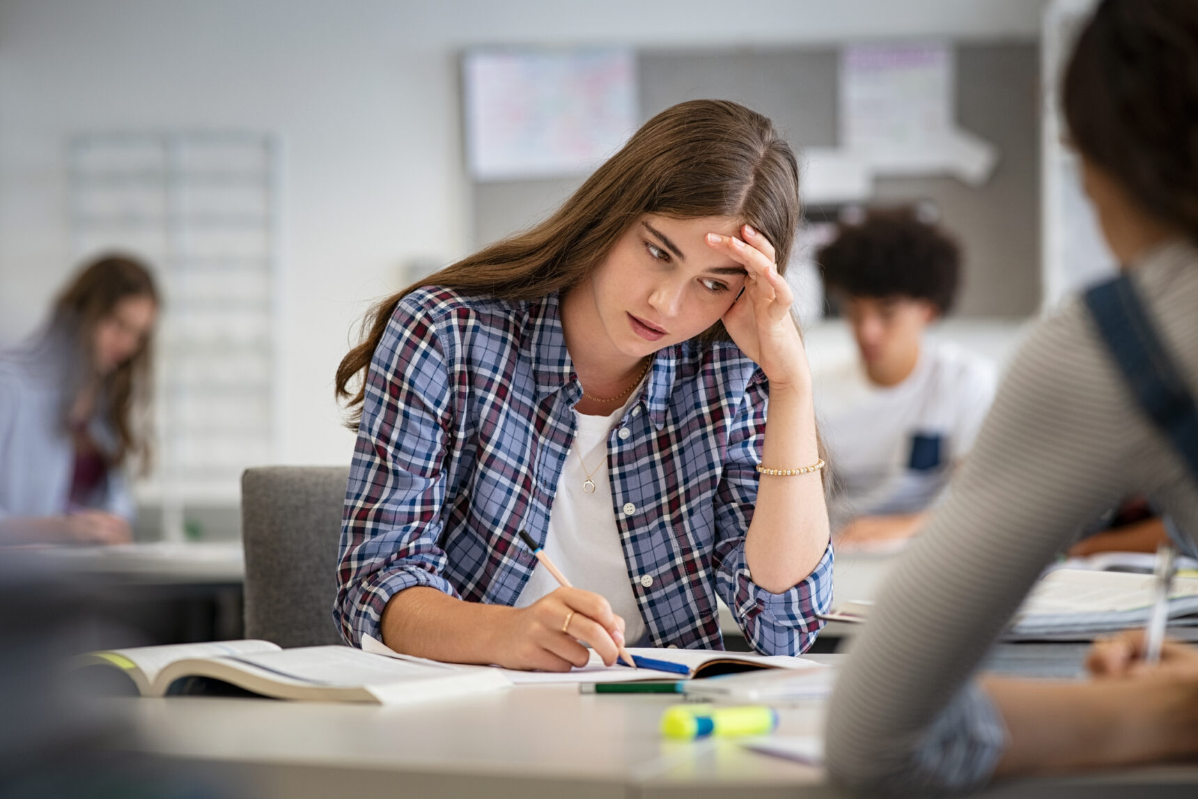 A female student with maths anxiety is sitting at a classroom desk hiding her face with her hand.