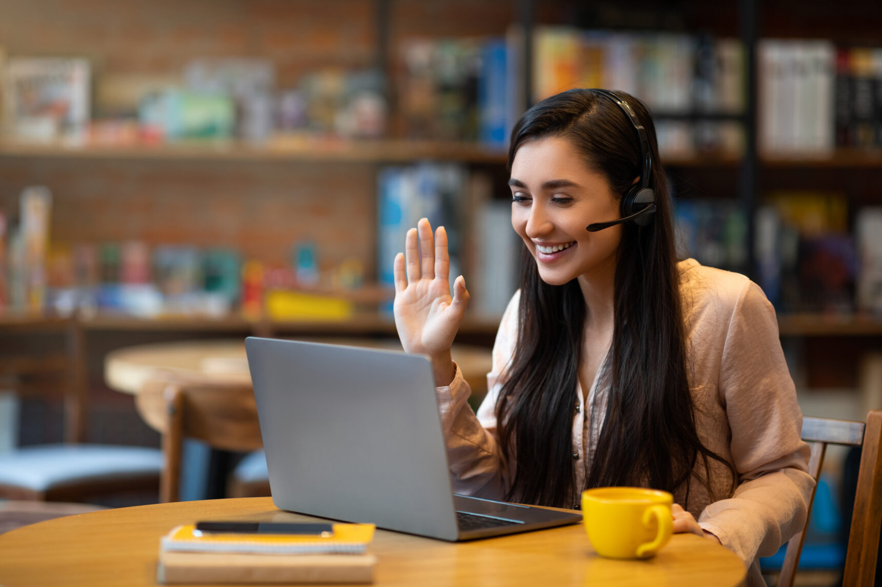 A female online tutor is waving at a student at the start of a tuition session.